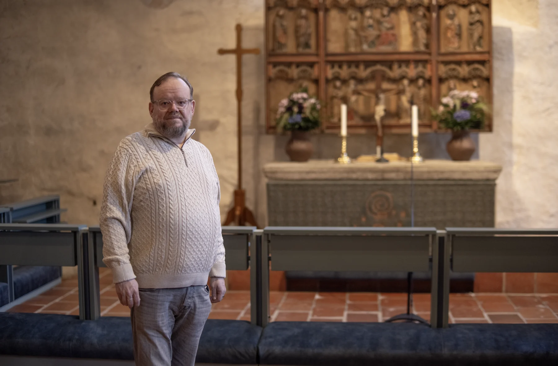Juha Säijälä kirkon sisällä alttarin edessä. Taustalla näkyvät risti, kynttilät ja alttarikaappi.