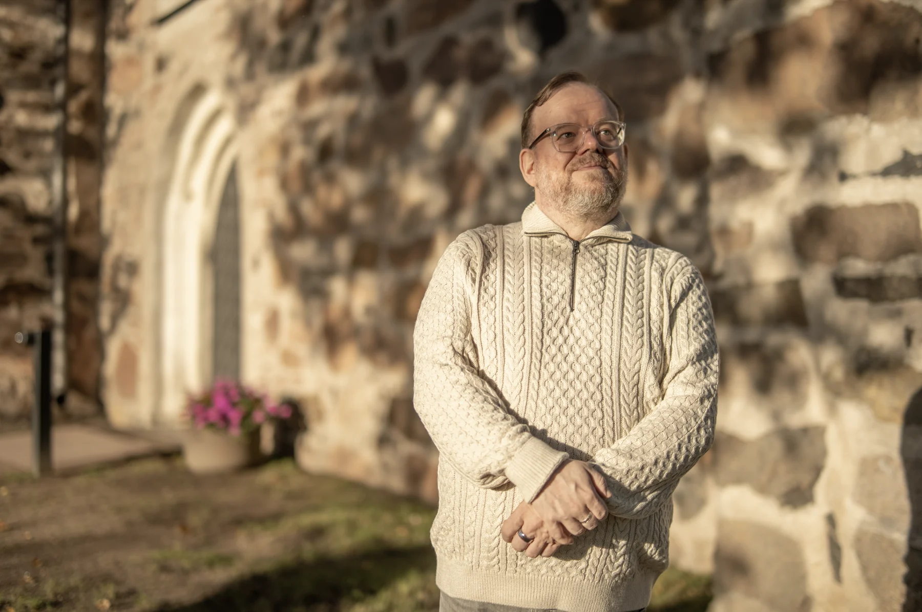 Juha Säijälä seisoo vaaleassa neuleessa kivikirkon seinustalla.